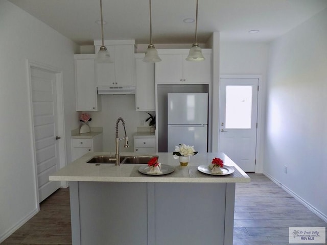 kitchen featuring white cabinets, pendant lighting, white refrigerator, and a center island with sink