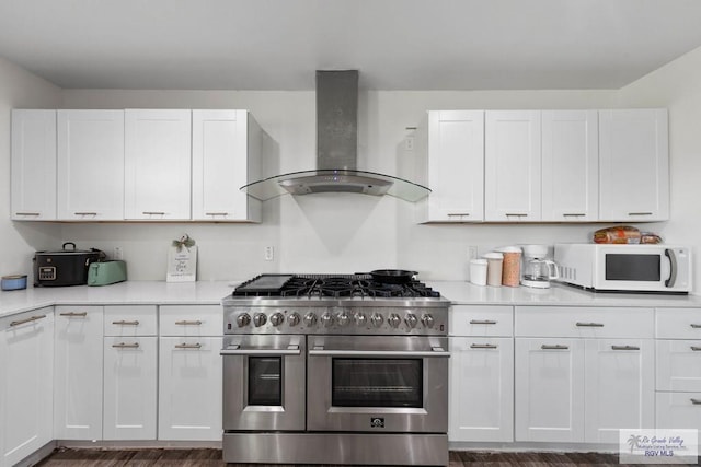 kitchen featuring dark wood-type flooring, wall chimney exhaust hood, range with two ovens, and white cabinets