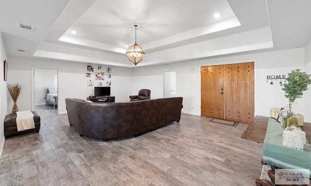 living room with an inviting chandelier, a tray ceiling, and hardwood / wood-style floors