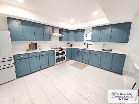 kitchen with a raised ceiling, a sink, wall chimney range hood, white fridge, and double oven range