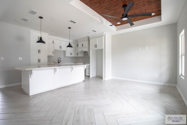 kitchen featuring visible vents, a raised ceiling, a breakfast bar area, light countertops, and white cabinetry