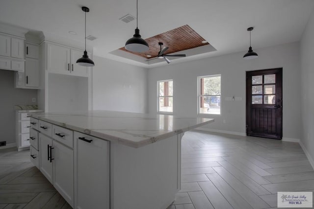 kitchen featuring visible vents, a raised ceiling, a kitchen island, light stone counters, and white cabinetry