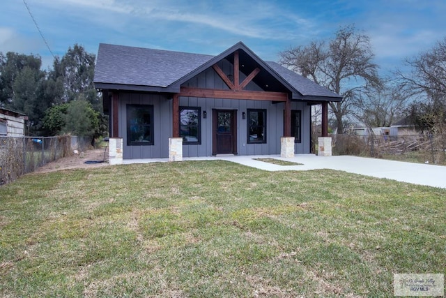 view of front facade with a porch, a shingled roof, fence, a front lawn, and board and batten siding