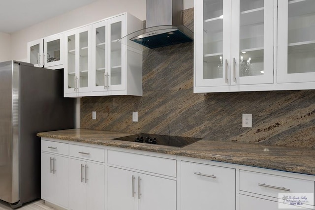 kitchen featuring stainless steel fridge, white cabinets, dark stone counters, decorative backsplash, and wall chimney range hood