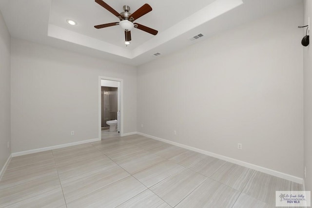 empty room featuring ceiling fan, a tray ceiling, and light tile patterned floors