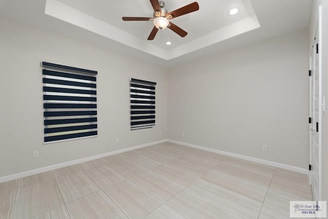 tiled empty room featuring ceiling fan and a raised ceiling