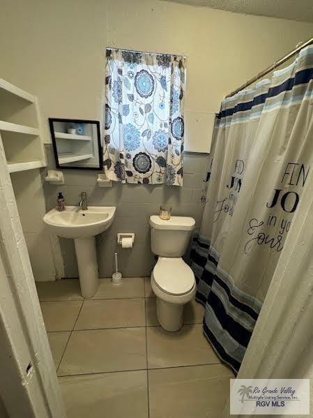 bathroom with sink, tile patterned flooring, a shower with shower curtain, toilet, and tile walls