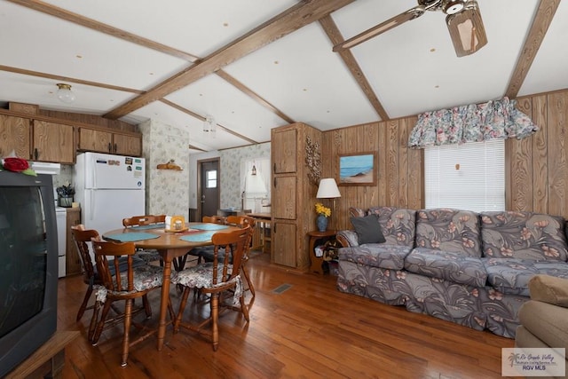 dining area with vaulted ceiling with beams, wood walls, hardwood / wood-style floors, and ceiling fan