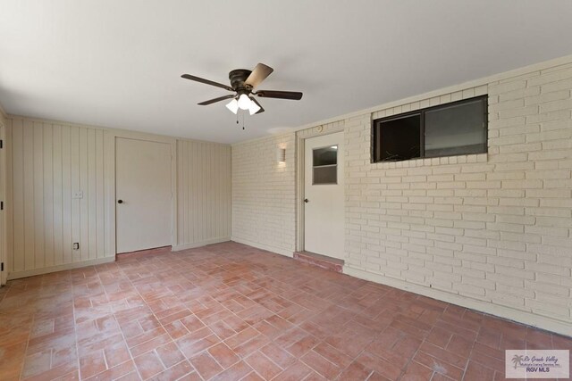 spare room with ceiling fan and brick wall