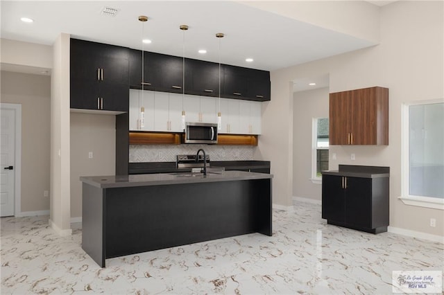 kitchen featuring pendant lighting, decorative backsplash, a center island with sink, and sink