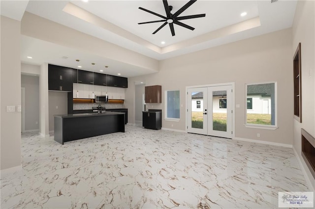 kitchen with a kitchen island with sink, a high ceiling, french doors, ceiling fan, and a tray ceiling