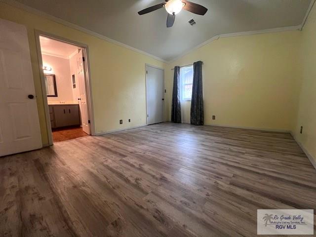 unfurnished bedroom with lofted ceiling, connected bathroom, ornamental molding, hardwood / wood-style flooring, and ceiling fan