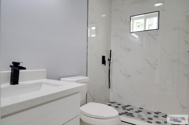 bathroom with a tile shower, vanity, and toilet