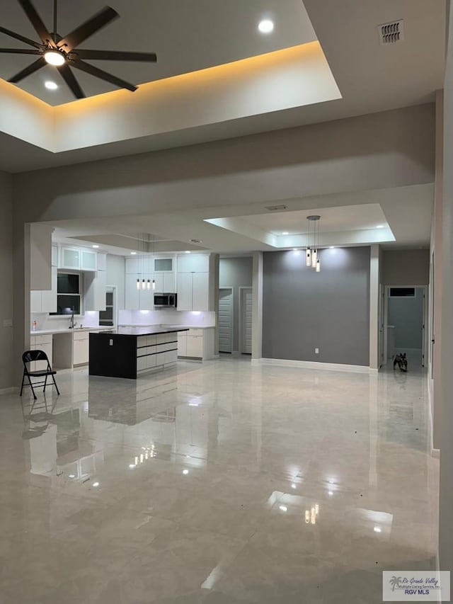 kitchen featuring a raised ceiling, ceiling fan, decorative light fixtures, white cabinets, and a large island