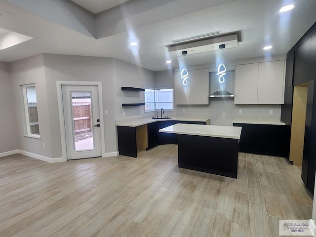 kitchen featuring white cabinetry, light hardwood / wood-style floors, a center island, wall chimney exhaust hood, and sink