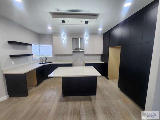 kitchen with white cabinets, a center island, wall chimney exhaust hood, decorative light fixtures, and sink