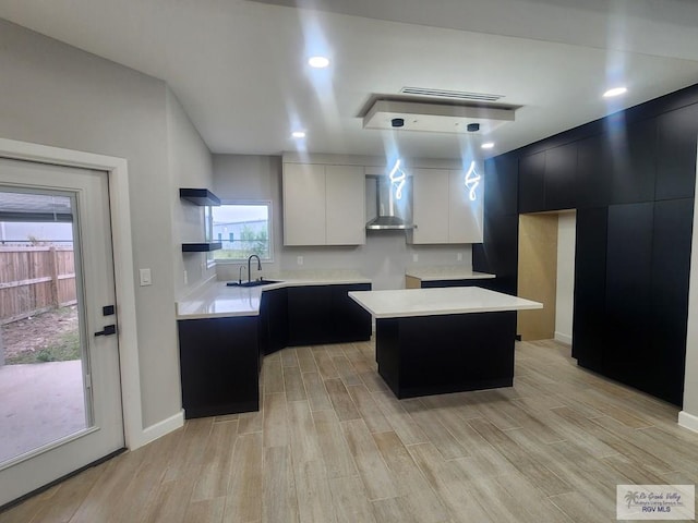 kitchen with pendant lighting, a center island, wall chimney exhaust hood, white cabinetry, and sink