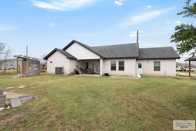 rear view of property featuring brick siding, a shingled roof, central AC unit, and a yard