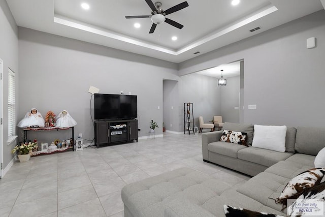 living area with a raised ceiling, visible vents, ceiling fan, and baseboards