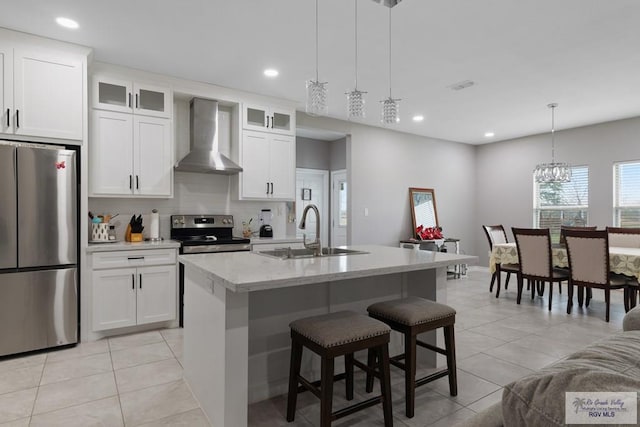 kitchen featuring light tile patterned floors, a center island with sink, wall chimney exhaust hood, stainless steel appliances, and a sink