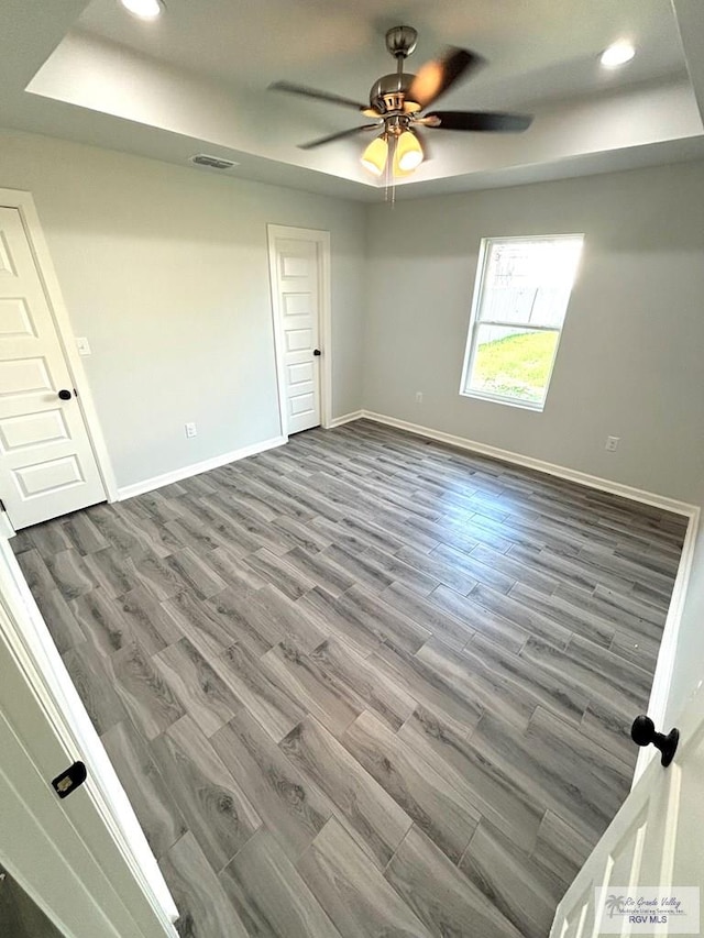 empty room with hardwood / wood-style floors, a raised ceiling, and ceiling fan