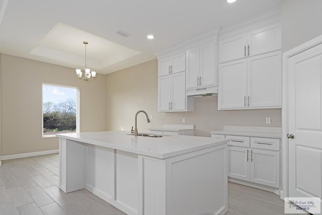 kitchen with a raised ceiling, sink, a center island with sink, white cabinetry, and hanging light fixtures