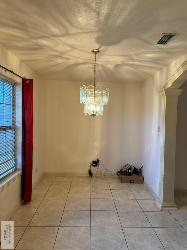 unfurnished dining area with ornate columns, light tile patterned floors, a textured ceiling, and a chandelier