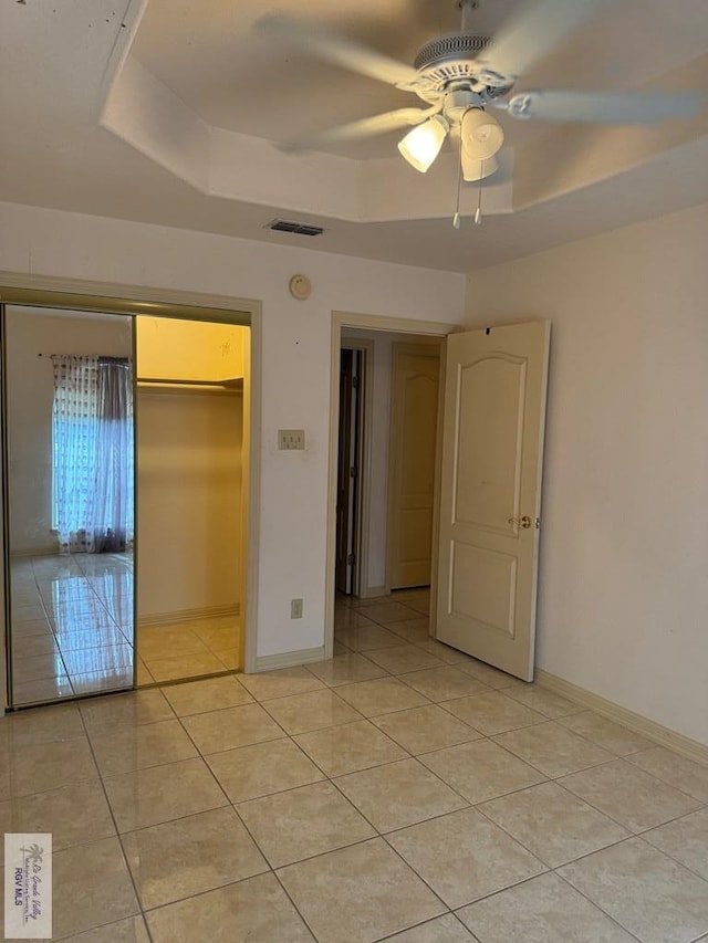 unfurnished bedroom featuring a raised ceiling, ceiling fan, and a closet