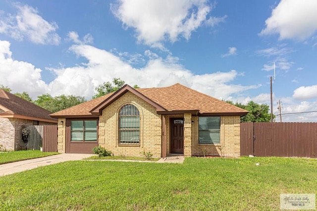 ranch-style house featuring brick siding, roof with shingles, a front yard, and fence
