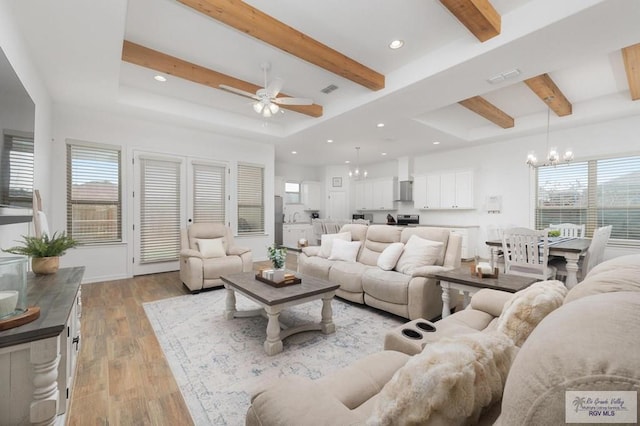 living room with beamed ceiling, a raised ceiling, ceiling fan with notable chandelier, and light hardwood / wood-style flooring