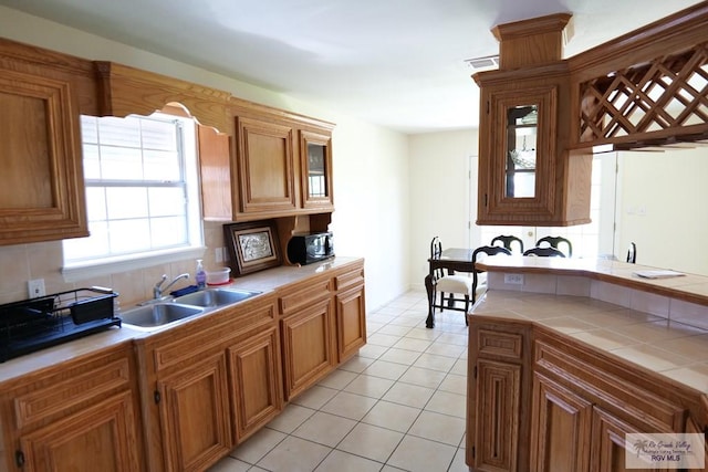 9165 Los Olmos Dr, Los Fresnos, TX 78566 - kitchen featuring tile countertops, light tile patterned floors, a sink, brown cabinetry, and backsplash