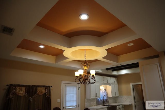 details featuring tasteful backsplash, coffered ceiling, sink, an inviting chandelier, and white cabinets