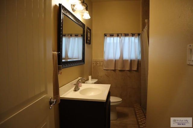 bathroom featuring walk in shower, vanity, tile walls, and toilet