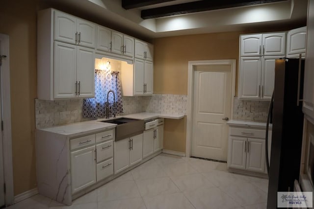 kitchen with decorative backsplash, sink, beamed ceiling, white cabinetry, and fridge