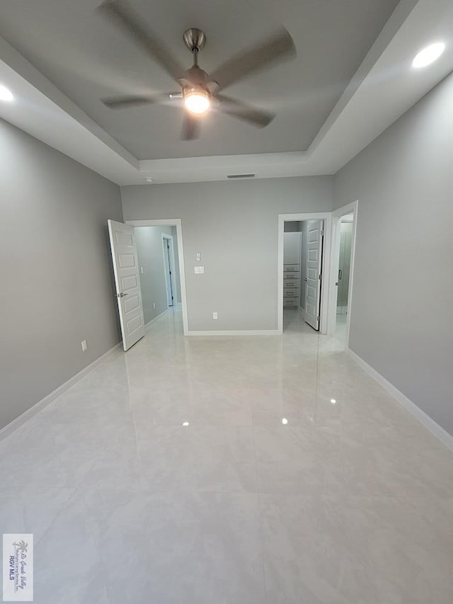 unfurnished bedroom featuring a tray ceiling, ceiling fan, and baseboards