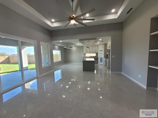 unfurnished living room featuring a tray ceiling, baseboards, and visible vents