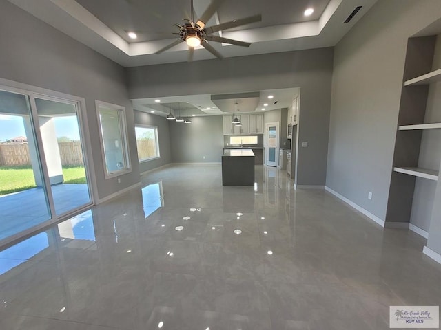unfurnished living room with visible vents, a tray ceiling, and baseboards