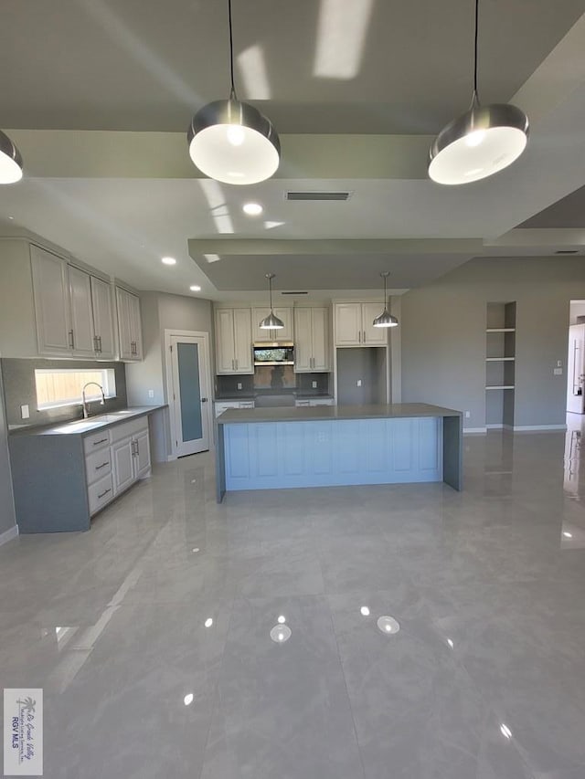kitchen with baseboards, visible vents, ventilation hood, a sink, and hanging light fixtures