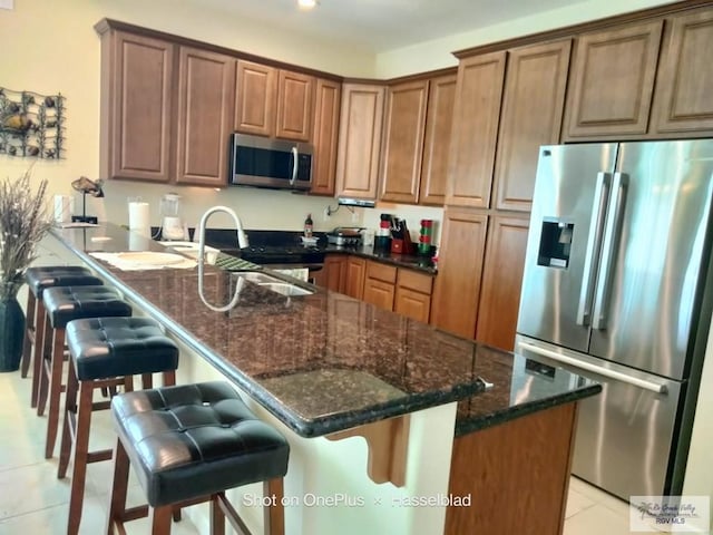 kitchen with light tile patterned flooring, a breakfast bar, a sink, dark stone countertops, and appliances with stainless steel finishes