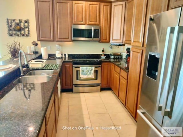 kitchen featuring brown cabinetry, a sink, dark stone counters, and stainless steel appliances