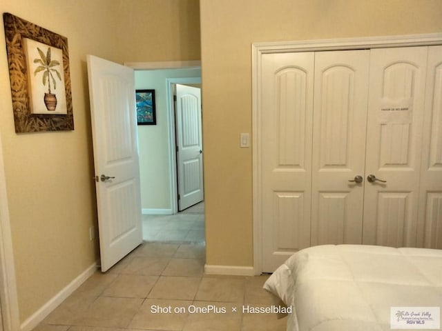 bedroom with baseboards, light tile patterned flooring, and a closet