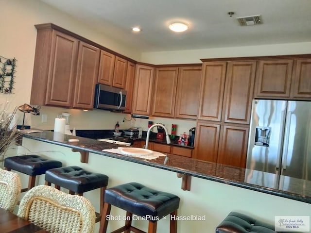 kitchen featuring dark stone counters, a breakfast bar area, stainless steel appliances, and visible vents