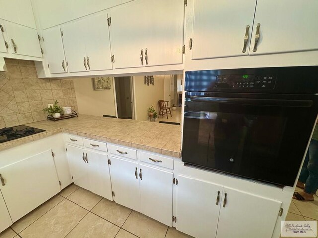 1901 Martha St, Harlingen, TX 78550 - kitchen featuring black appliances, light tile patterned floors, backsplash, light countertops, and white cabinets