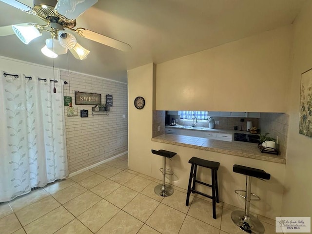1901 Martha St, Harlingen, TX 78550 - kitchen with brick wall, a ceiling fan, a breakfast bar area, light tile patterned flooring, and backsplash