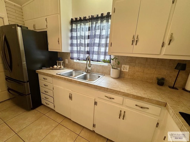1901 Martha St, Harlingen, TX 78550 - kitchen featuring freestanding refrigerator, decorative backsplash, white cabinetry, and light tile patterned floors
