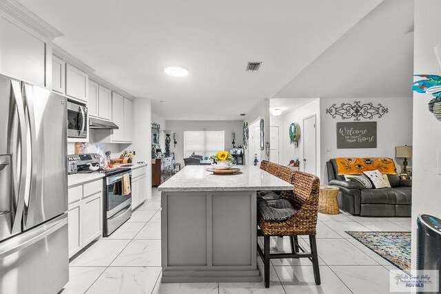 kitchen with a breakfast bar, a center island, white cabinets, light stone countertops, and appliances with stainless steel finishes