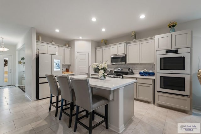 kitchen with sink, appliances with stainless steel finishes, a kitchen island with sink, a kitchen breakfast bar, and tasteful backsplash