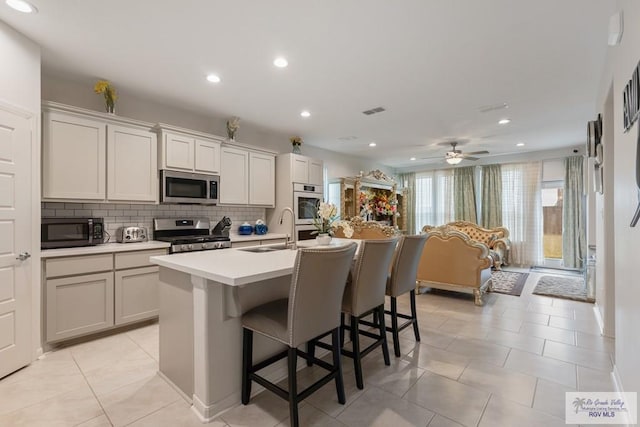 kitchen featuring appliances with stainless steel finishes, tasteful backsplash, sink, a kitchen bar, and a center island with sink