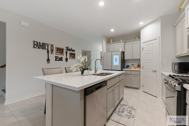 kitchen featuring sink, backsplash, a kitchen breakfast bar, stainless steel appliances, and a center island with sink