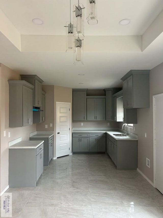 kitchen featuring gray cabinetry, sink, pendant lighting, and a raised ceiling